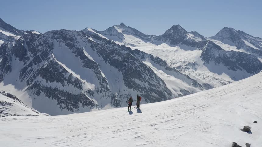 A pair of mountaineers standing high in the mountains look out over the snowy landscape