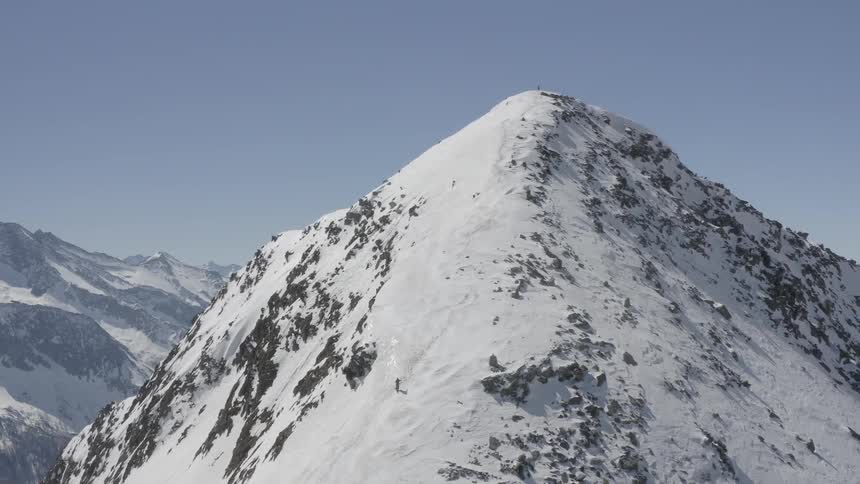 A person is hiking up a steep sloped mountain ridge that is covered in snow
