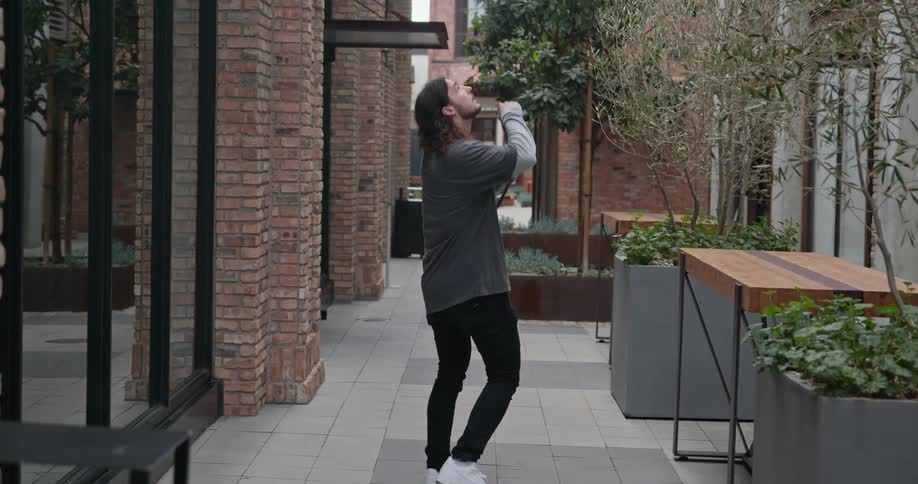 Male photographer walks along narrow gap between buildings stopping to take a picture