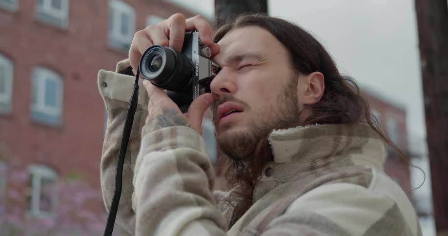 Male photographer lifts camera to eye and takes picture while standing across street from an apartment building