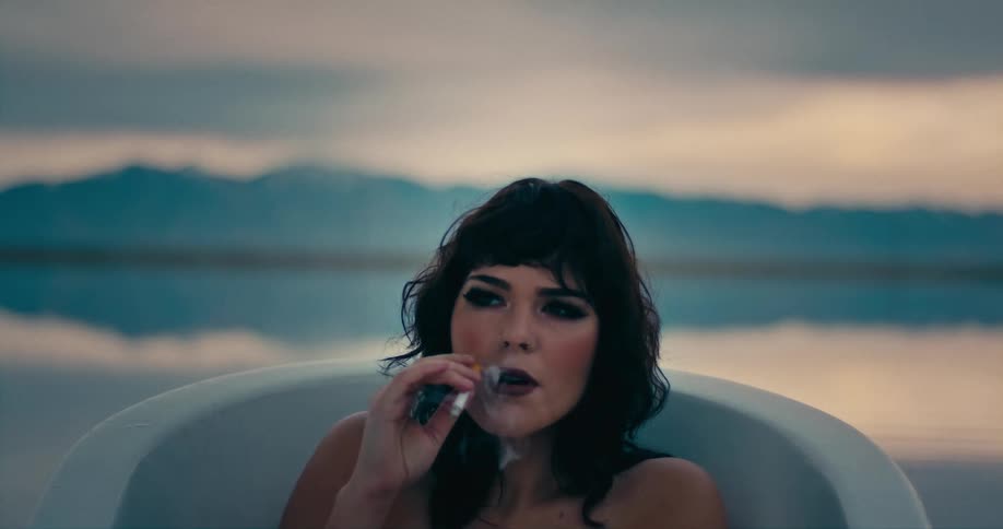 A woman smokes a cigarette while sitting in an outdoor bathtub