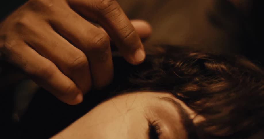 A man is caressing the face and hair of a woman who is laying down