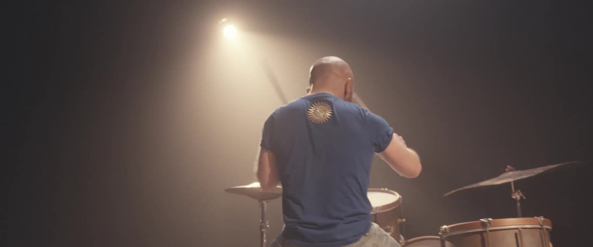 A man is holding drumsticks and playing the drums as a light shines above him