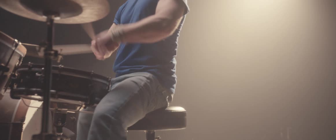 A man sitting on a stool on stage playing the drums