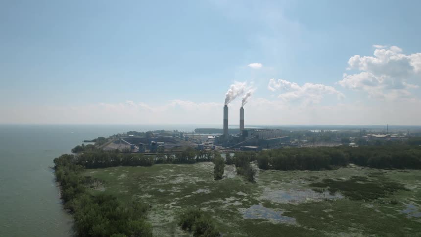 Aerial view of two chimney stacks on a factory spewing smoke near the coast
