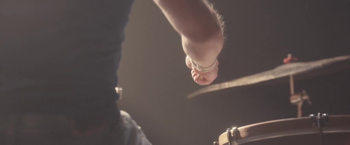 A man is holding drumsticks and playing the drums as a light shines above him