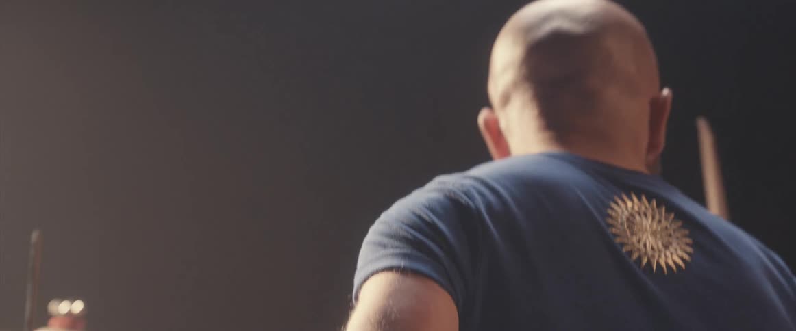 A drummer plays the drums under a spotlight in a dark place