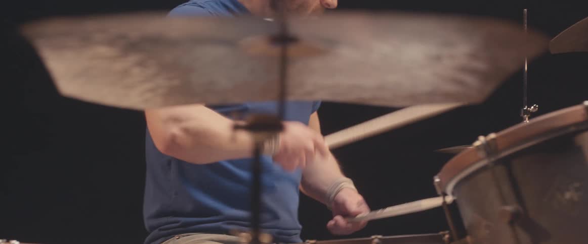 A musician is holding drumsticks and keeping the rhythm playing the drums and cymbals