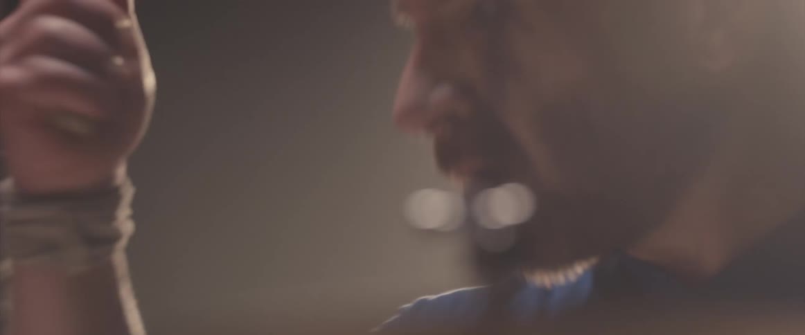 Bald male drummer with blue shirt and beard plays drums in spotlight