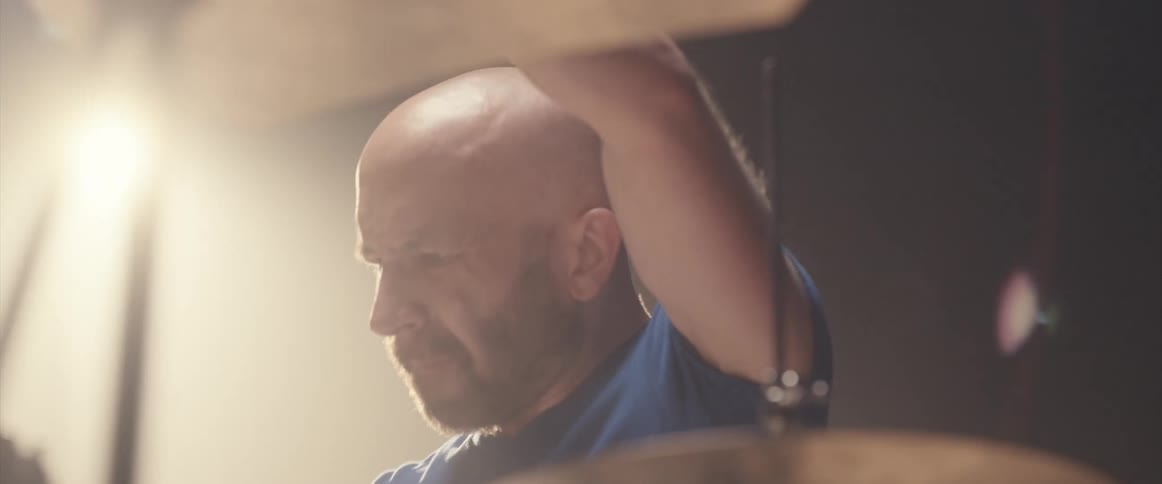 Bald muscular man playing drums on a stage under a spotlight