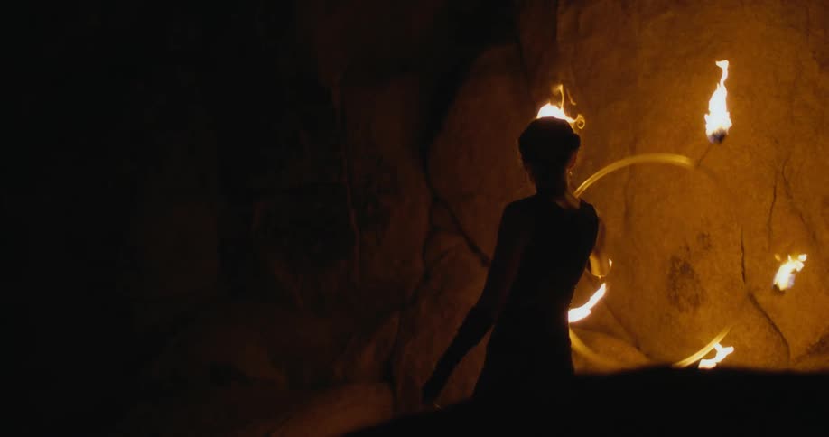 A woman dances with a ring of fire in a cave