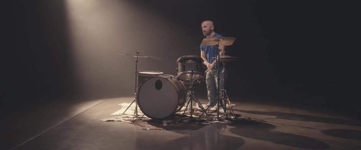 A drummer finishes a song and stands up and walks away from his drums carrying his drum sticks