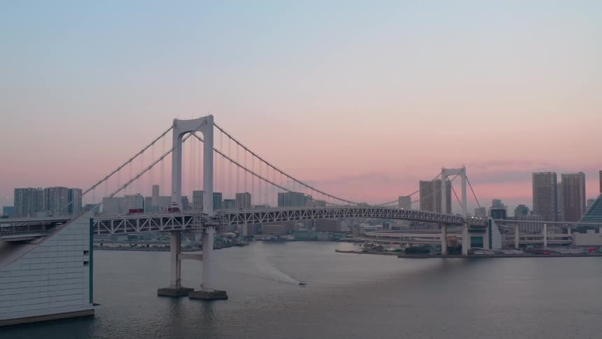 Suspension bridge over a river in front of a city skyline at evening