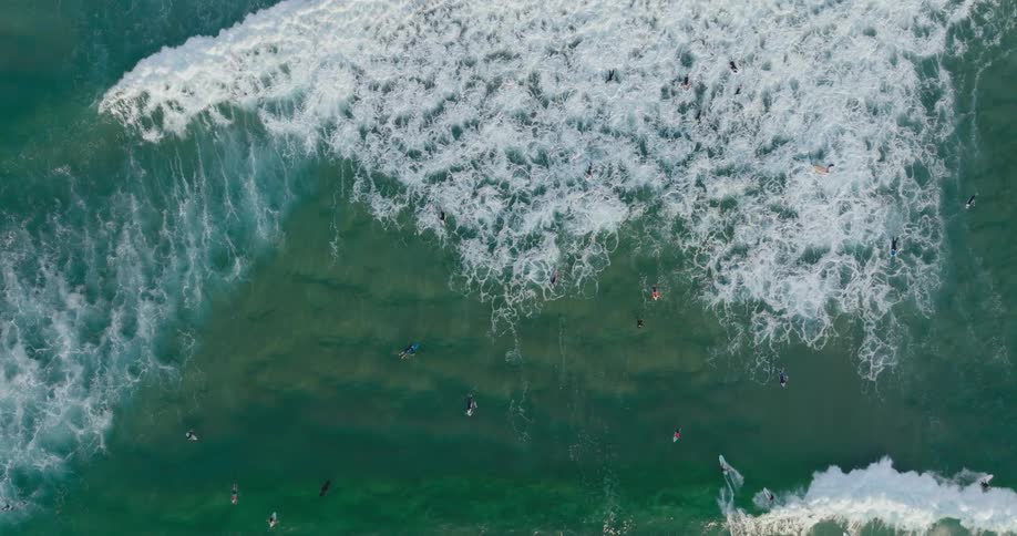 Top down aerial view of surfers floating over the green waves in the ocean
