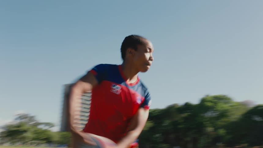 A group of girls are running and playing rugby on a sports field on a sunny day