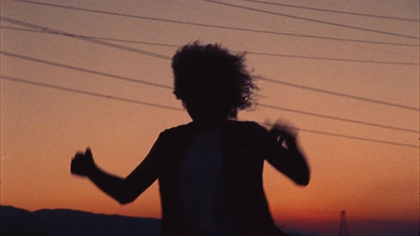 A woman dances outdoors in the countryside at sunset