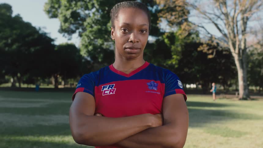 Female athlete stands in park with arms crossed