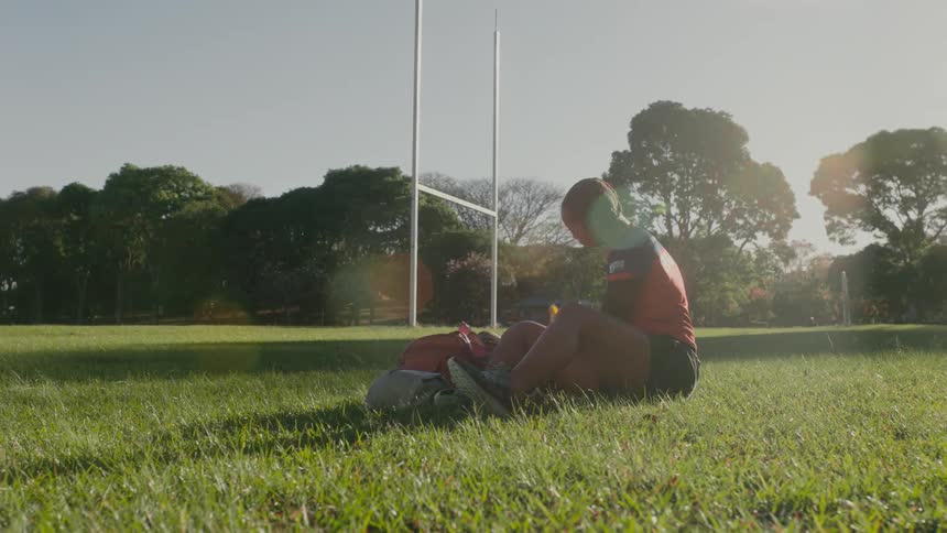A female athlete sits on the grass field and gets her shoes ready