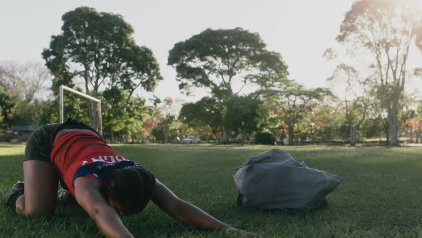 A woman in a sports uniform does stretches on an athletics field during the day