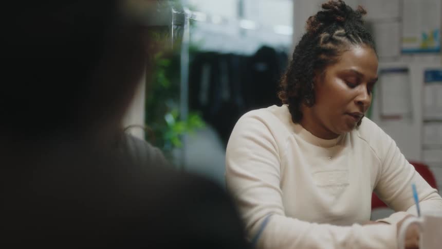 A woman talks with the people sitting with her at a table while writing