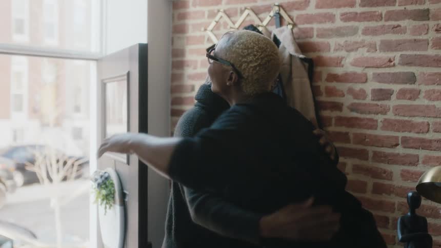Young woman greets elderly woman at the front door with a smile and a hug