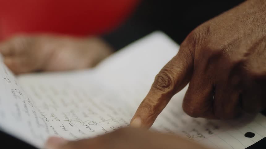 A black woman is holding a letter in her hands and moving her finger across the paper as she reads