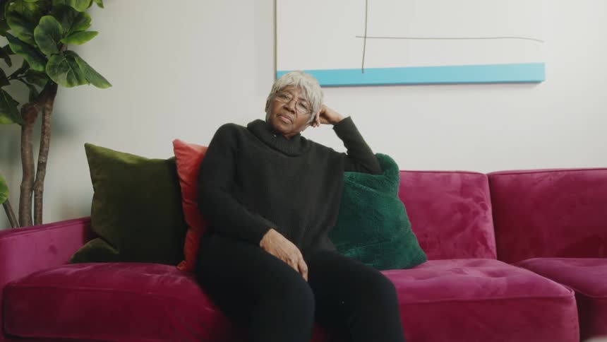 Mature woman wearing black clothes sitting on a fuchsia couch at home