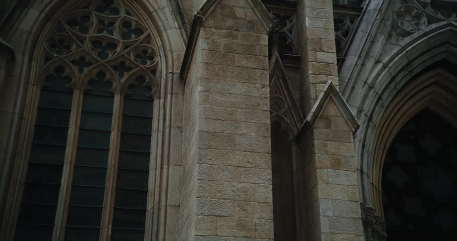 A church with ornate windows and doorways sits below skyscrapers downtown