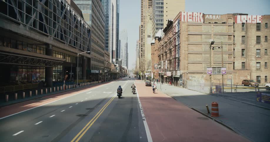 People on motorcycles are traveling on a city street surrounded by tall buildings