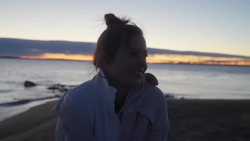 A young woman smiles and laughs while standing on a beach near the ocean