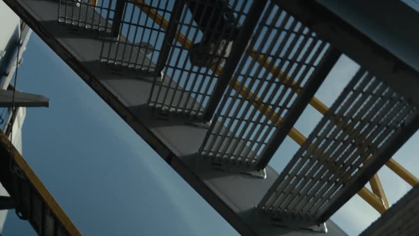 A person can be seen ascending a metallic staircase that is located outdoors