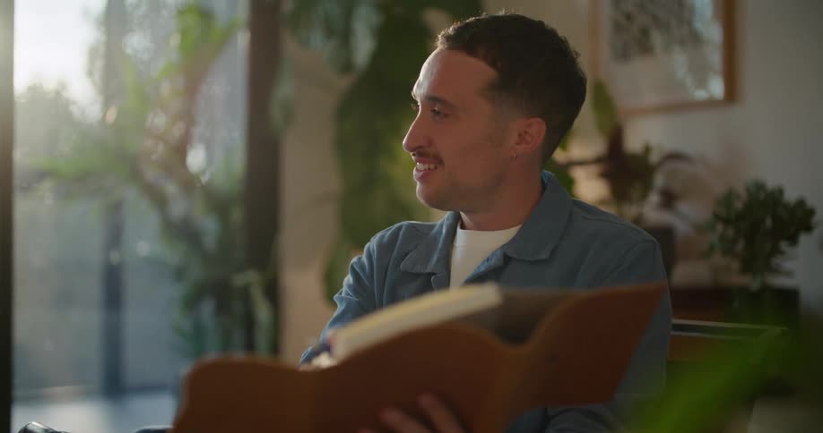 Man sits in room talking while referencing book