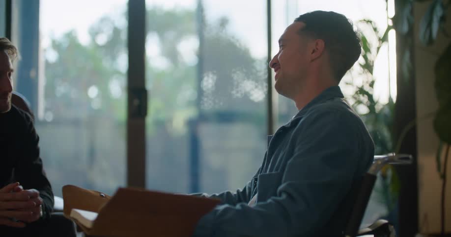 Two men chat over a book while sitting at home