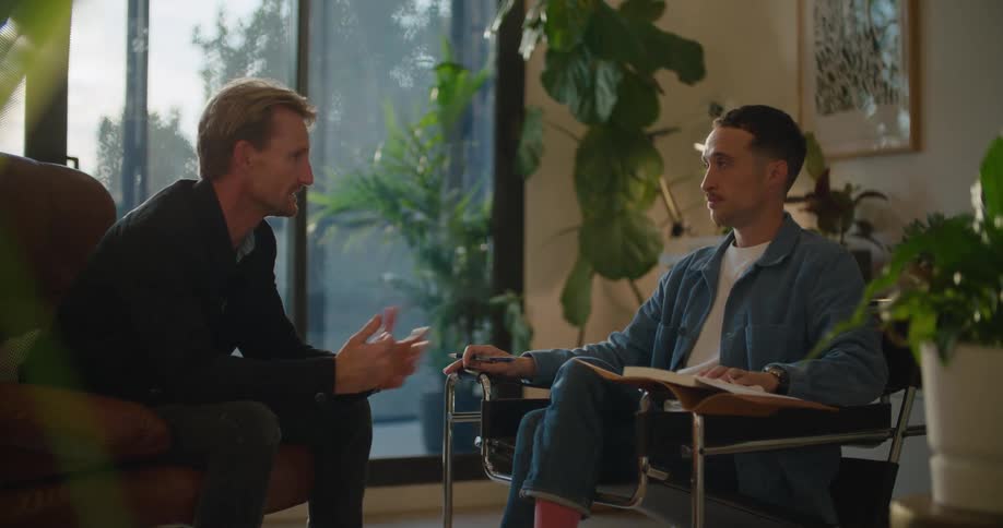 Two men sit having a discussion in area containing many houseplants