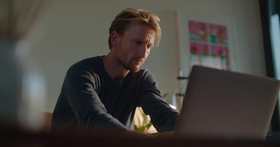 A man uses a laptop while sitting indoors during the day
