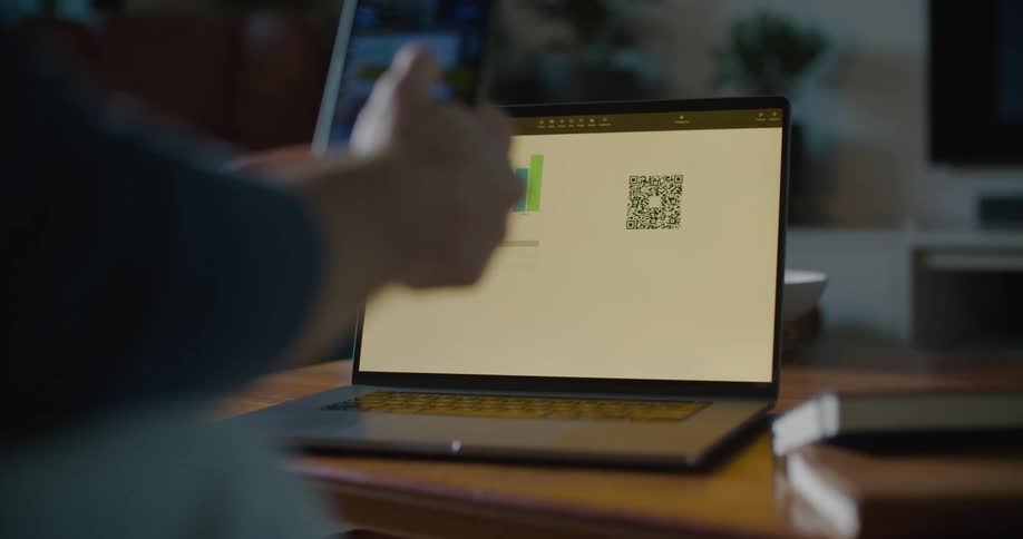 A person is seated with their laptop on a coffee table in front of them while they hold their cell phone