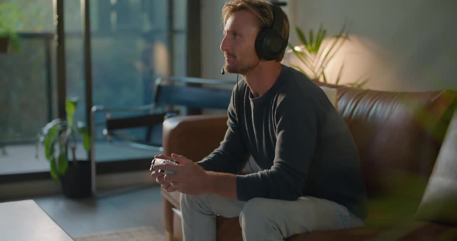 A man talking on a headset while playing a video game leans back and yells in frustration