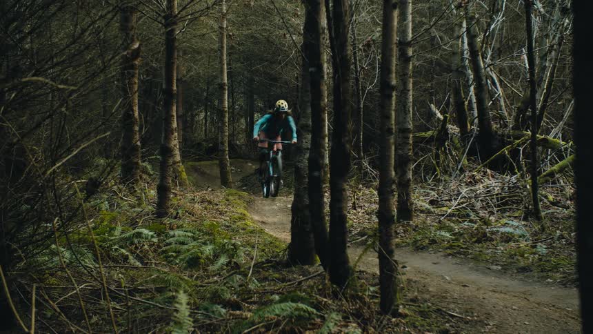 A woman wearing a helmet is riding a bike on a trail in the woods