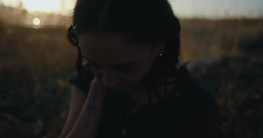 Woman sits in fields as sun shines past mountains on the horizon