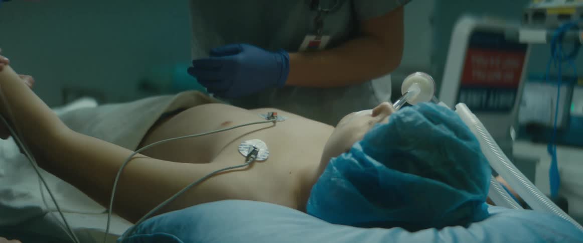 Doctors are working on a young patient who is hooked up to machines in a hospital room