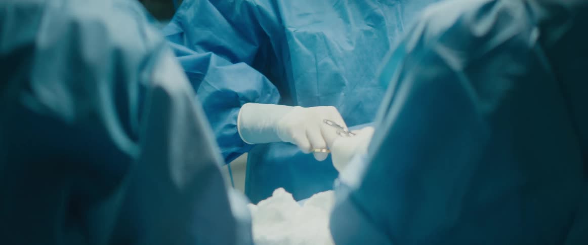 A doctor is performing surgery on a patient and two others wearing blue gowns are present