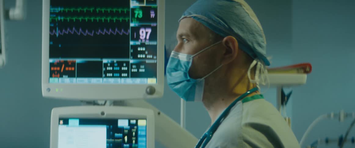 Doctor wearing scrubs stands near ekg and other medical machinery