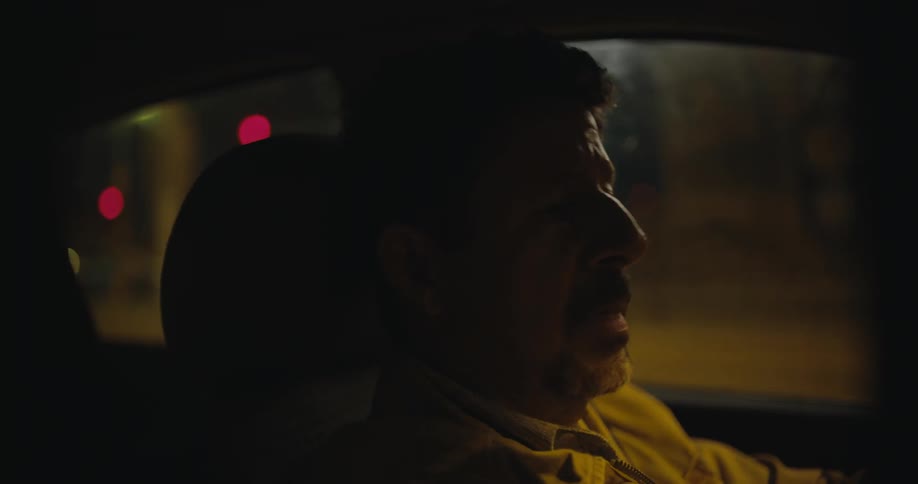A man is driving an automobile at night and he appears to be tired