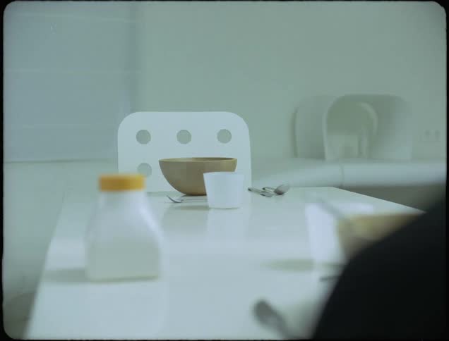 A sterile white table and empty chair with a large bowl and utensils