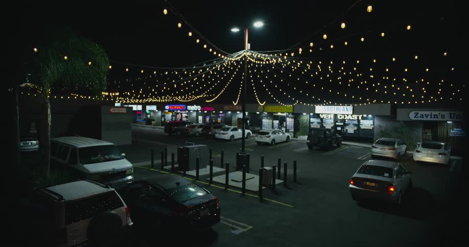 Car leaves the parking lot of a small shopping center at night