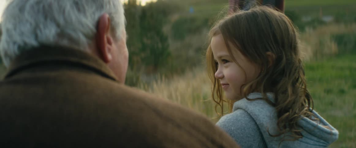 A man sitting in the grass on a slope talking to his granddaughter