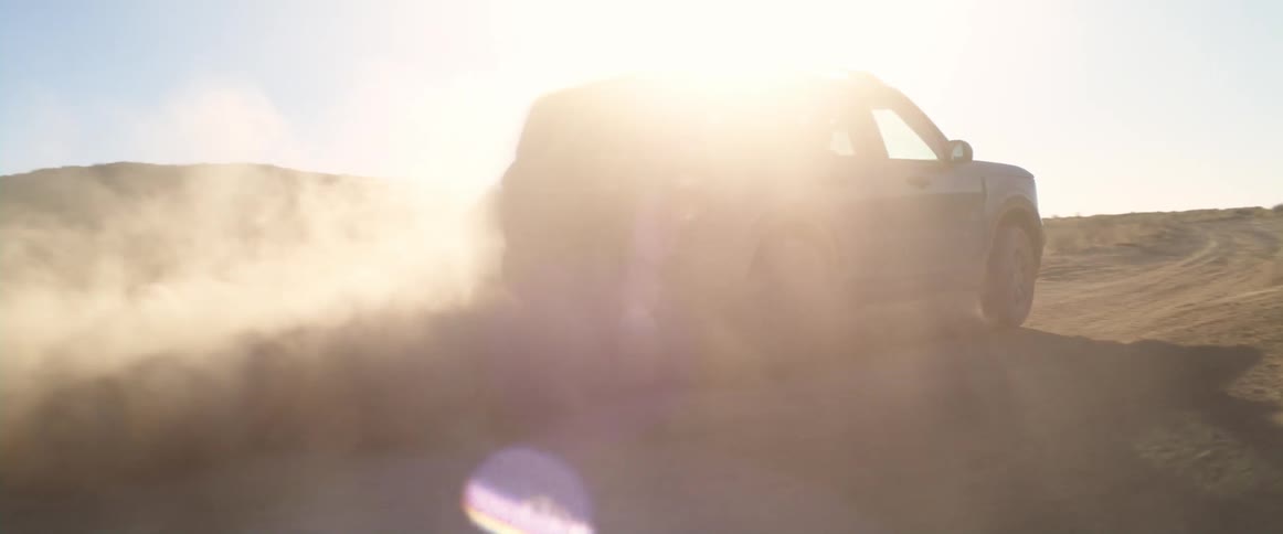 A sports utility vehicle is driven through a desert landscape and kicks up a large cloud of dust behind it