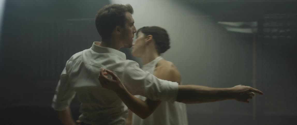 A man and woman perform a modern dance under a flashing light on stage