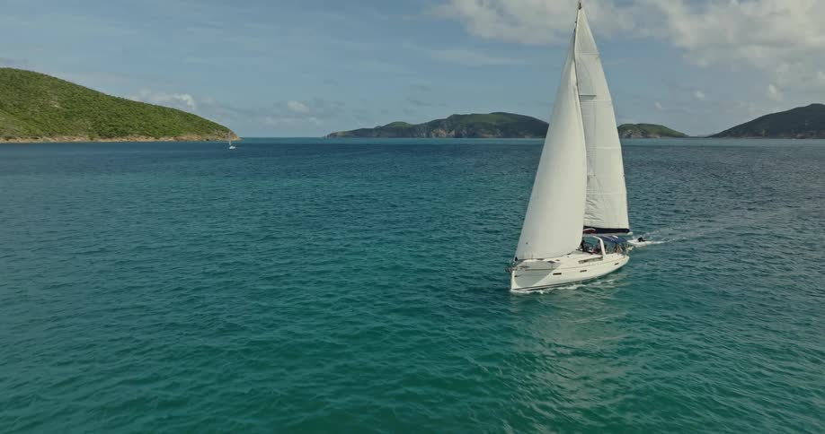 A sailboat pulls a person on a surfboard in the ocean
