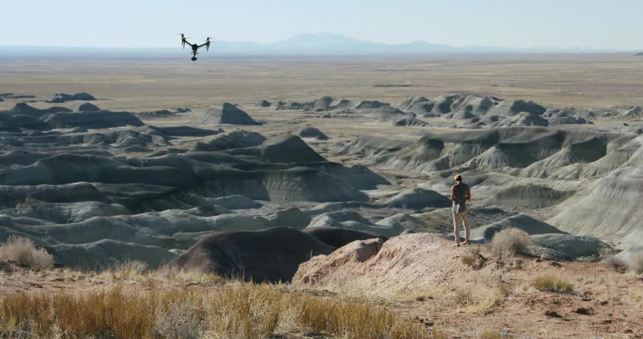 A man is standing in the desert operating a drone